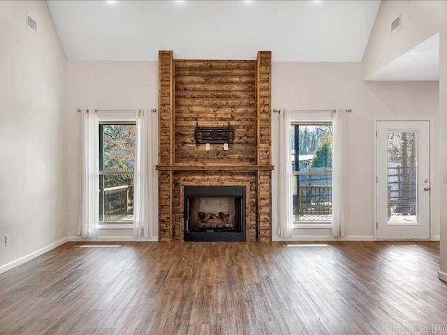 unfurnished living room featuring a fireplace, visible vents, vaulted ceiling, and dark wood finished floors