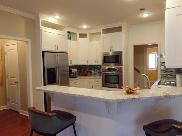 kitchen with a peninsula, appliances with stainless steel finishes, visible vents, and light stone countertops