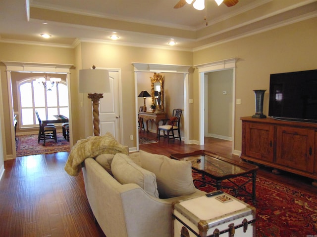 living area with dark wood-style floors, crown molding, baseboards, and ceiling fan with notable chandelier