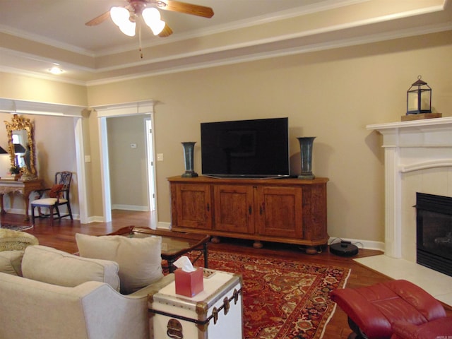 living area featuring ornamental molding, a tray ceiling, baseboards, and a tile fireplace