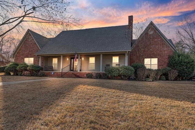 view of front of property featuring covered porch, a yard, brick siding, and a chimney