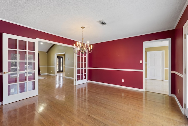 empty room featuring french doors, visible vents, a textured ceiling, wood finished floors, and a chandelier