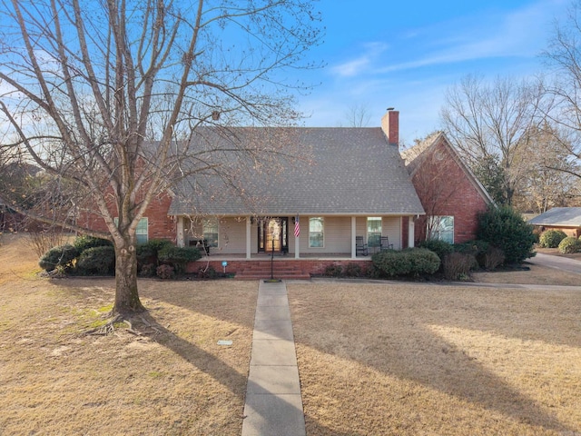 view of front of home with a porch, brick siding, a shingled roof, a front lawn, and a chimney