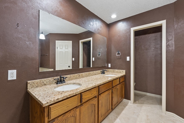 full bath featuring double vanity, a textured ceiling, baseboards, and a sink