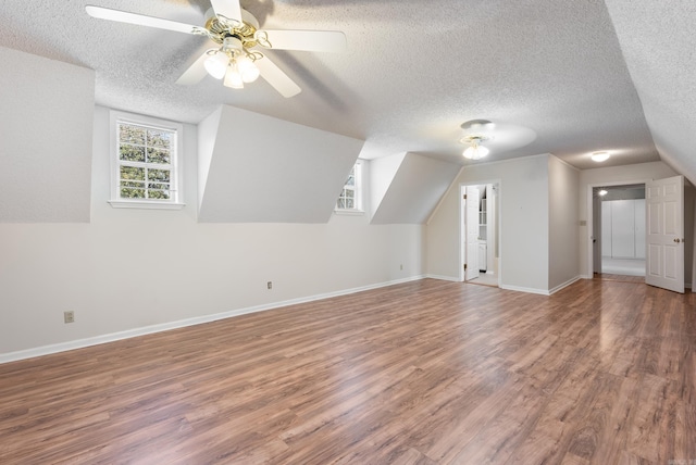 bonus room with lofted ceiling, a textured ceiling, wood finished floors, a ceiling fan, and baseboards