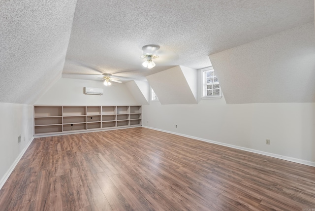 bonus room featuring dark wood-type flooring, a wall unit AC, vaulted ceiling, and baseboards