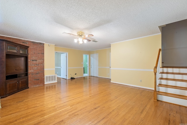 unfurnished living room featuring a textured ceiling, light wood-style flooring, visible vents, stairs, and crown molding