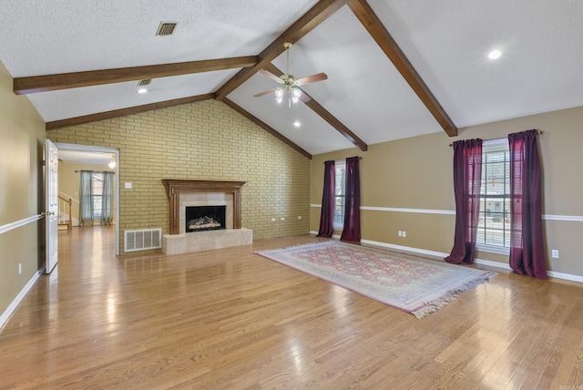 unfurnished living room featuring a large fireplace, visible vents, lofted ceiling with beams, a textured ceiling, and light wood-type flooring