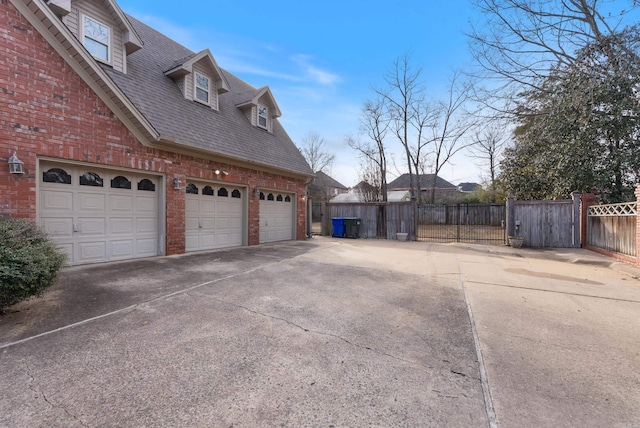 view of side of home featuring brick siding, roof with shingles, concrete driveway, fence, and a garage