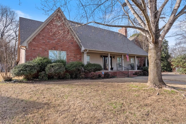 view of front of home featuring a shingled roof, a front yard, brick siding, and a chimney