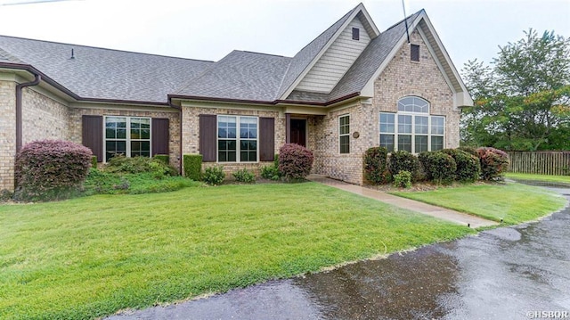 view of front facade with brick siding, roof with shingles, fence, and a front yard