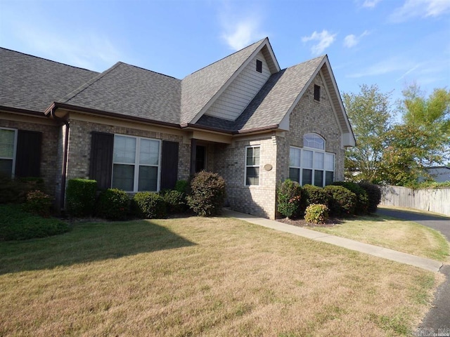 view of front facade with a shingled roof, brick siding, fence, and a front lawn