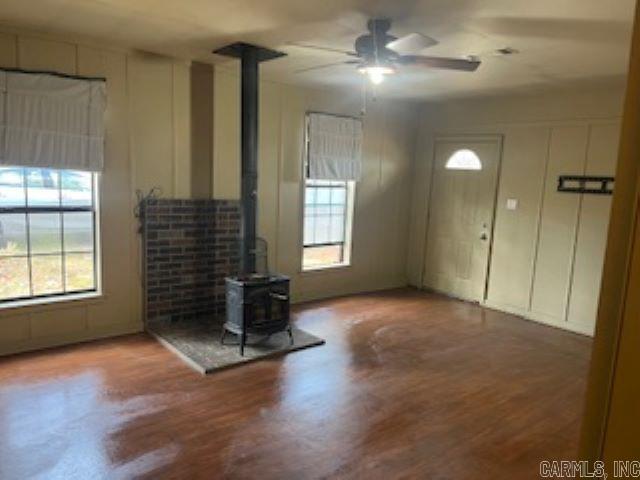 unfurnished living room with a wealth of natural light, a wood stove, ceiling fan, and wood finished floors