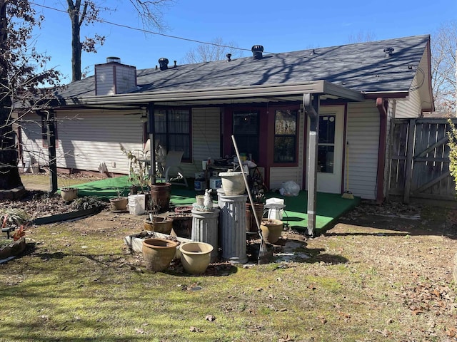 back of property with a shingled roof, a chimney, fence, and a lawn