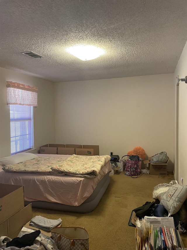 bedroom with a textured ceiling, visible vents, and carpet flooring