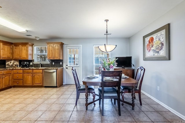 kitchen featuring baseboards, decorative backsplash, dishwasher, brown cabinets, and decorative light fixtures