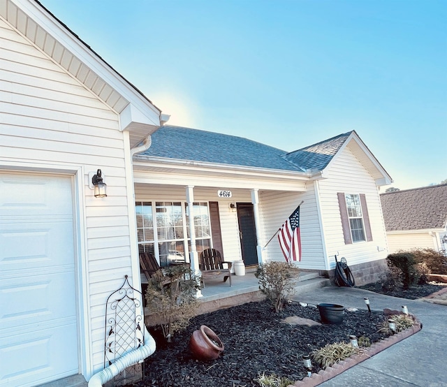 doorway to property featuring covered porch, roof with shingles, and a garage