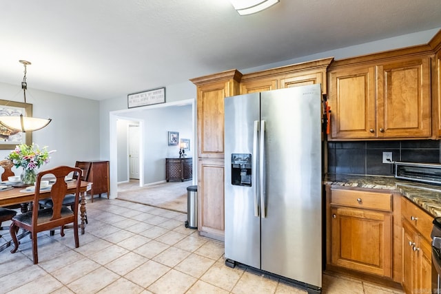 kitchen with pendant lighting, brown cabinets, stainless steel refrigerator with ice dispenser, decorative backsplash, and dark stone counters