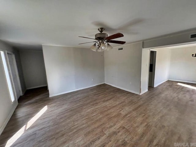 spare room featuring baseboards, visible vents, a ceiling fan, ornamental molding, and dark wood-style flooring