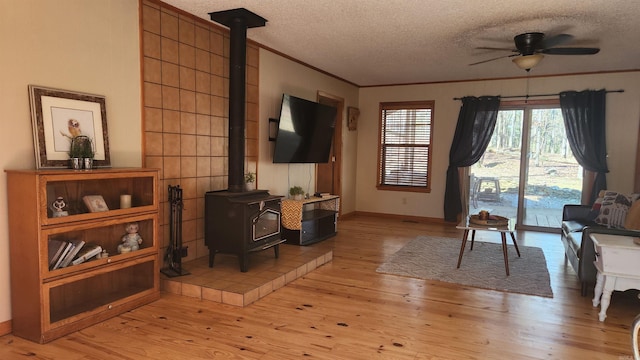 sitting room featuring a wood stove, light wood-style flooring, a textured ceiling, and crown molding