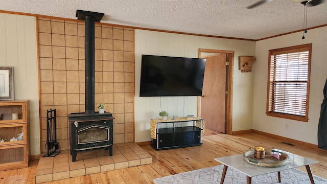 living room with a wood stove, light wood finished floors, ornamental molding, and a textured ceiling