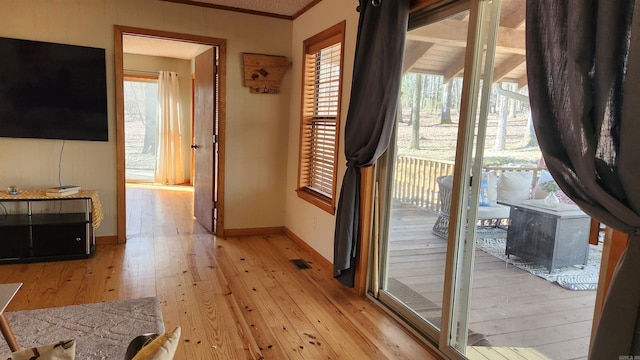 doorway with a wealth of natural light, light wood-type flooring, visible vents, and crown molding