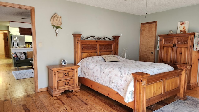 bedroom with a textured ceiling, light wood-type flooring, stainless steel refrigerator with ice dispenser, and baseboards