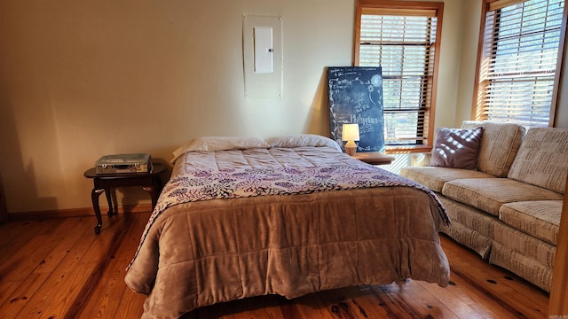 bedroom with wood finished floors, electric panel, and baseboards