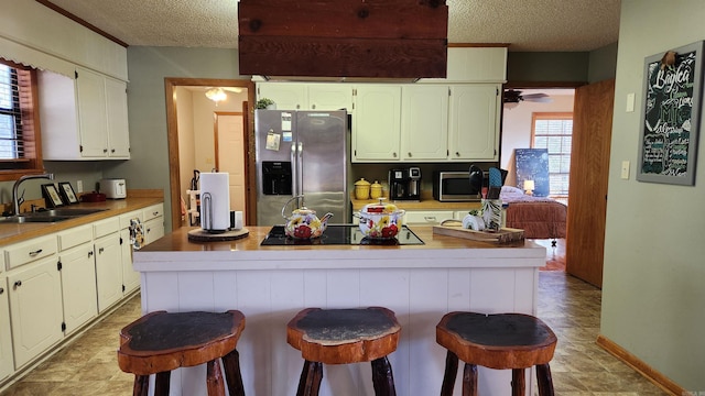 kitchen with a kitchen island, a sink, a kitchen breakfast bar, light countertops, and appliances with stainless steel finishes