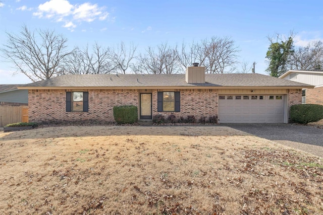 single story home with an attached garage, driveway, a chimney, and brick siding