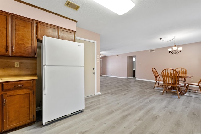 kitchen with visible vents, brown cabinets, light countertops, and freestanding refrigerator