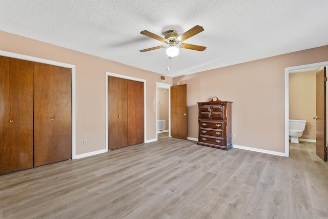 unfurnished bedroom with a textured ceiling, visible vents, baseboards, light wood-type flooring, and two closets