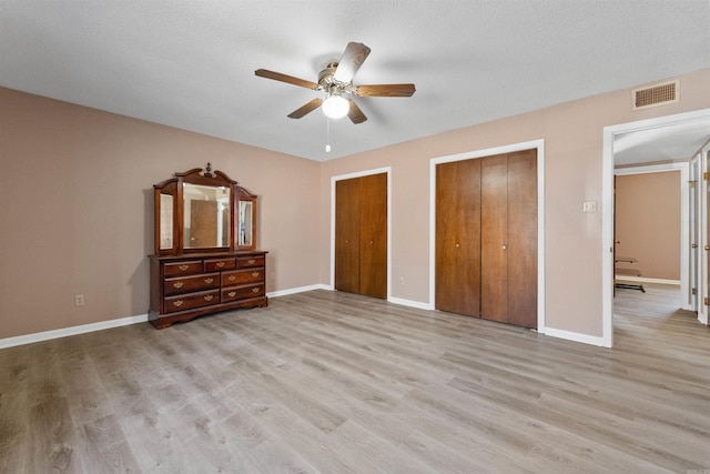 unfurnished bedroom featuring two closets, visible vents, light wood-style floors, ceiling fan, and baseboards