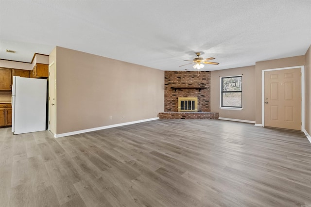 unfurnished living room featuring baseboards, a brick fireplace, light wood-style flooring, and a ceiling fan