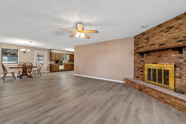 unfurnished living room with a textured ceiling, ceiling fan with notable chandelier, a fireplace, wood finished floors, and baseboards