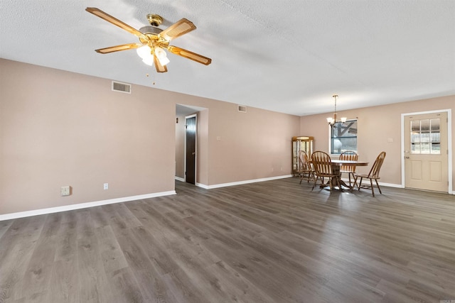 unfurnished dining area featuring dark wood-style flooring, visible vents, a textured ceiling, baseboards, and ceiling fan with notable chandelier