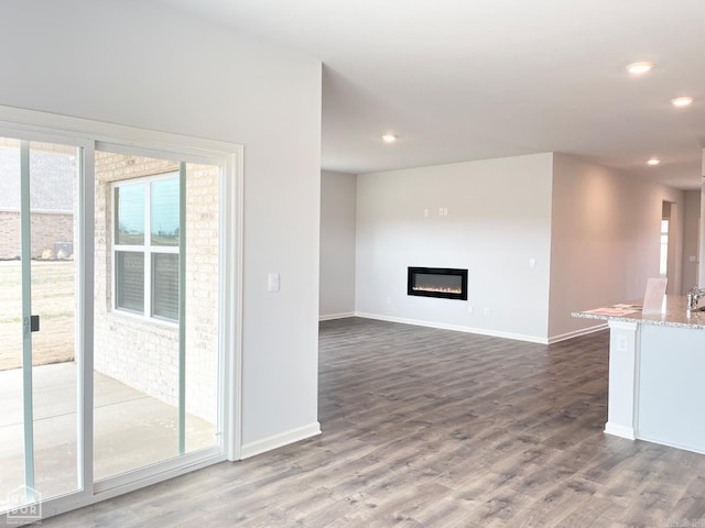 unfurnished living room with dark wood-style flooring, recessed lighting, a glass covered fireplace, and a healthy amount of sunlight