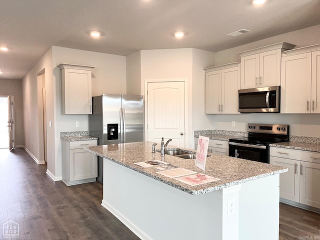 kitchen featuring stainless steel appliances, a sink, visible vents, dark wood-style floors, and a center island with sink