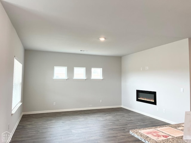 unfurnished living room featuring visible vents, baseboards, dark wood-style flooring, and a glass covered fireplace