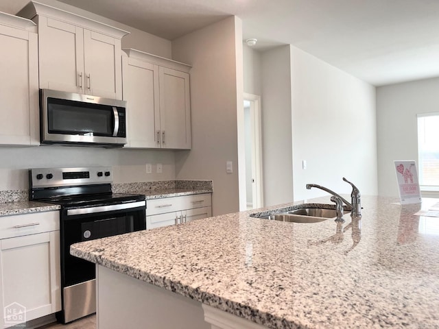 kitchen with white cabinetry, appliances with stainless steel finishes, light stone counters, and a sink