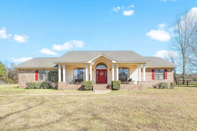 single story home with covered porch, roof with shingles, a front lawn, and brick siding