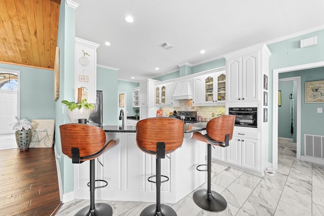 kitchen featuring a peninsula, visible vents, white cabinetry, black oven, and glass insert cabinets