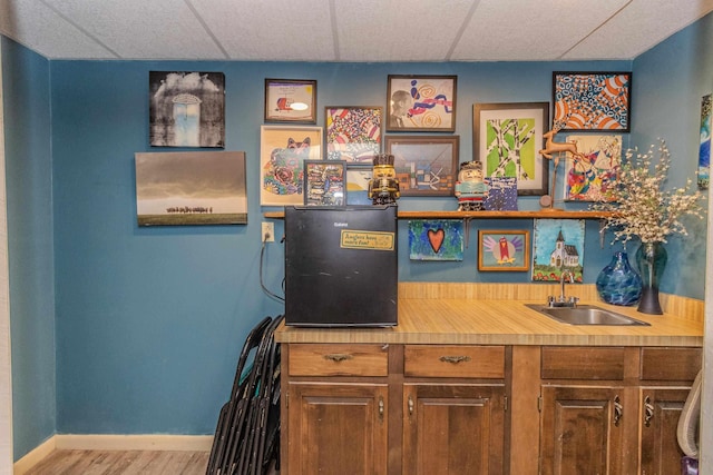 bar with a paneled ceiling, wet bar, wood finished floors, a sink, and baseboards