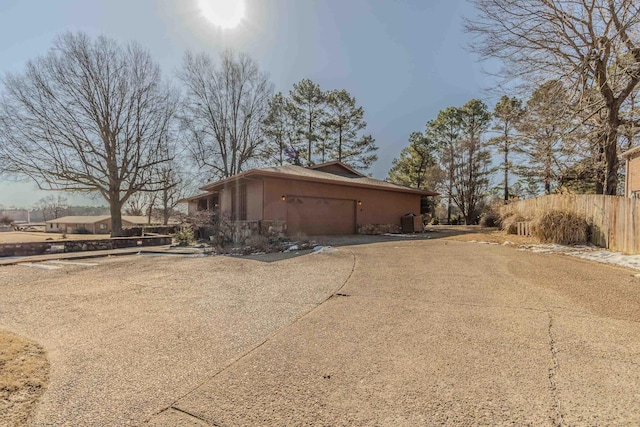 view of side of property with an attached garage, aphalt driveway, stucco siding, and fence