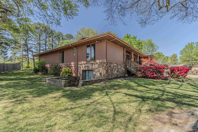 view of side of home featuring fence, stone siding, and a lawn