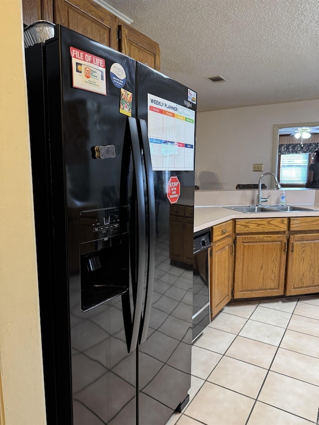 kitchen featuring brown cabinets, light countertops, light tile patterned flooring, a sink, and black appliances