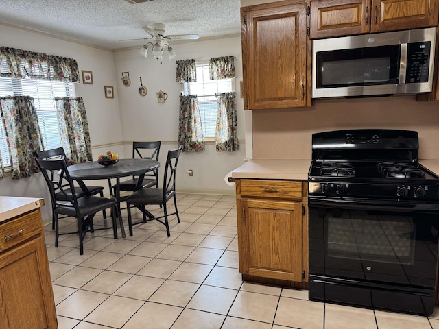 kitchen with brown cabinets, light countertops, stainless steel microwave, black range with gas cooktop, and a textured ceiling