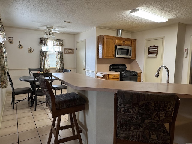 kitchen featuring light tile patterned floors, stainless steel microwave, brown cabinets, light countertops, and gas stove