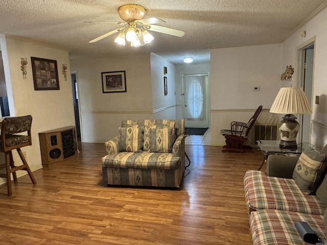 living room featuring a ceiling fan, crown molding, a textured ceiling, and wood finished floors