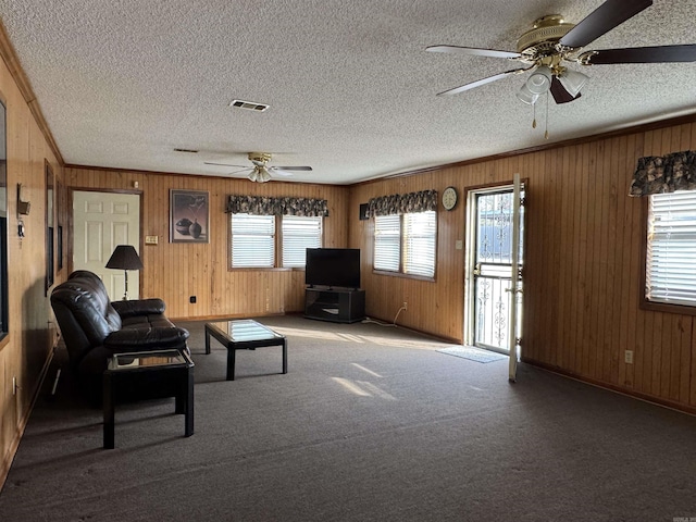 unfurnished living room featuring visible vents, a textured ceiling, crown molding, carpet floors, and wood walls